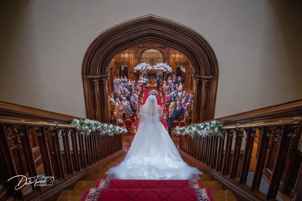 Bride from behind walking down the staircase to the wedding ceremony at Allerton Castle.