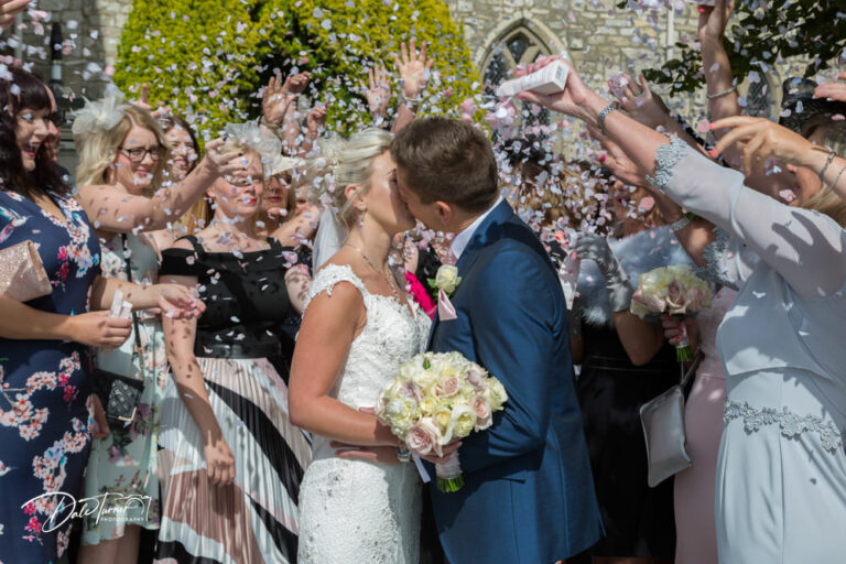 Bride and groom kissing and being covered in confetti, at Hazlewood Castle.