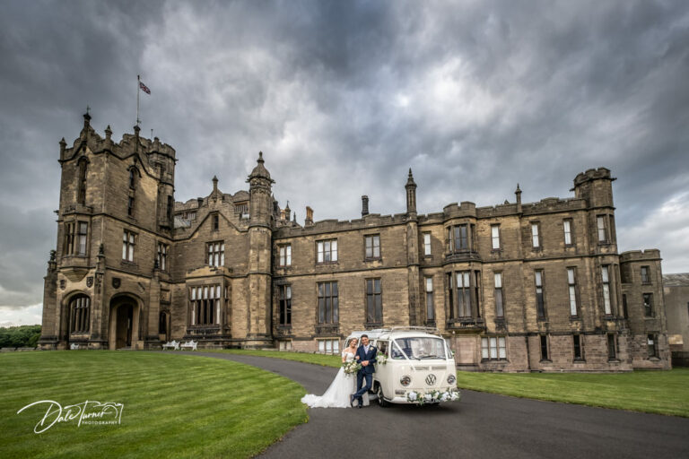 Bride and groom with a VW Camper at Allerton Castle with dark grey storm clouds above them.