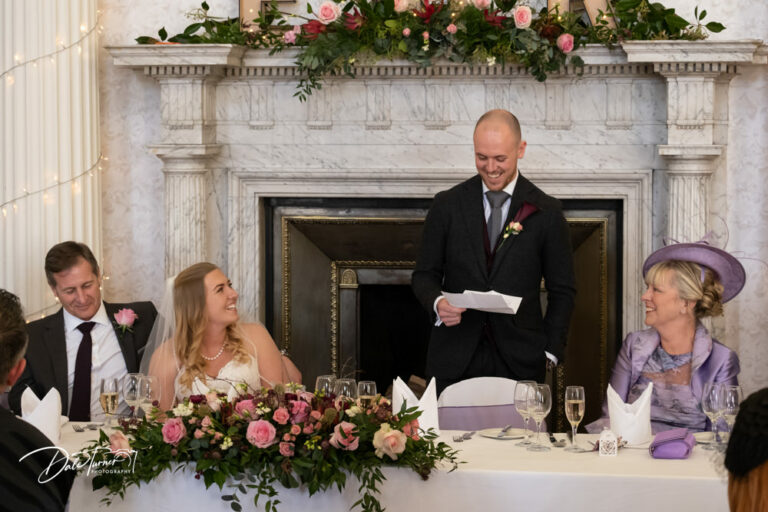 Groom giving a speech at the wedding reception and his bride is laughing. At Hazlewood Castle.
