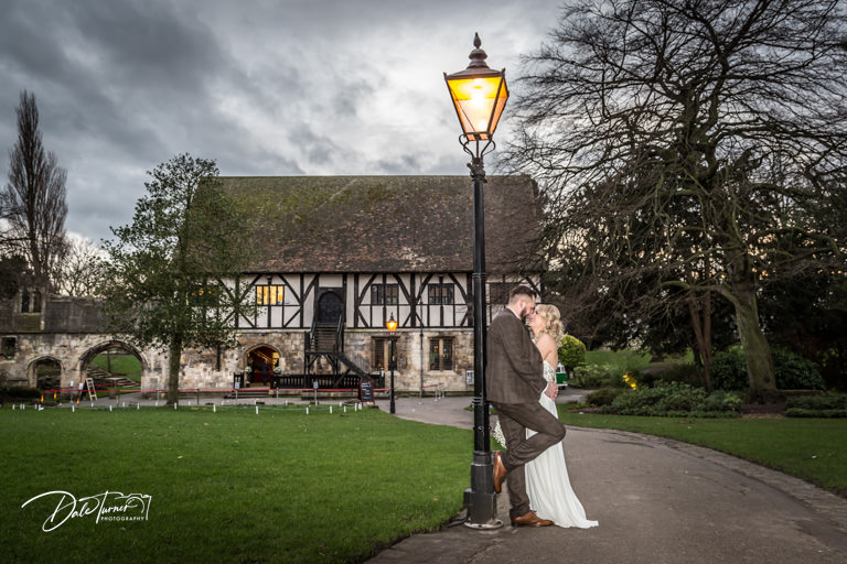 Bride and groom leaning against a lamp post outside the Hospitium, in the Museum Gardens in York.