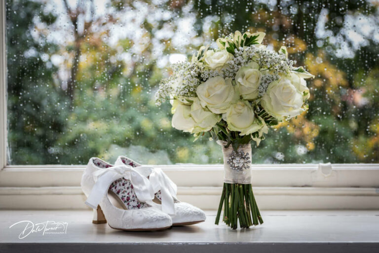 Wedding shoes and bouquet on a windowsill, with raindrops on the glass.