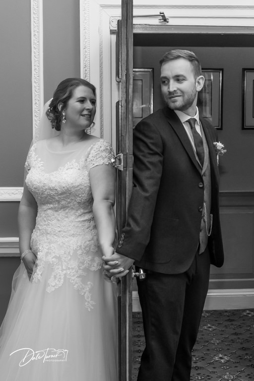 Bride and groom holding hands with a door between them.