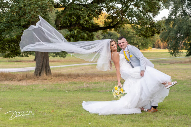 Bride and groom, leaning over with a long veil blowing in the wind. In the grounds of Carlton Towers.