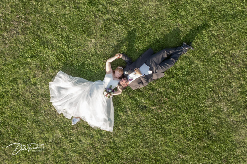 Drone image of bride and groom laying on grass.