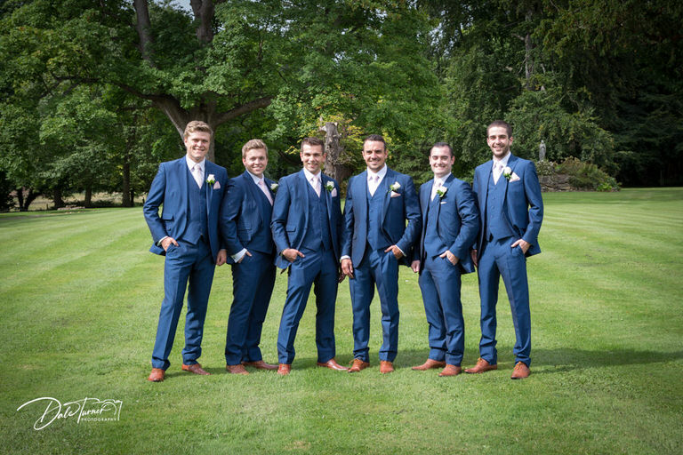 A groom and groomsmen lined up in the grounds of Hazlewood Castle.