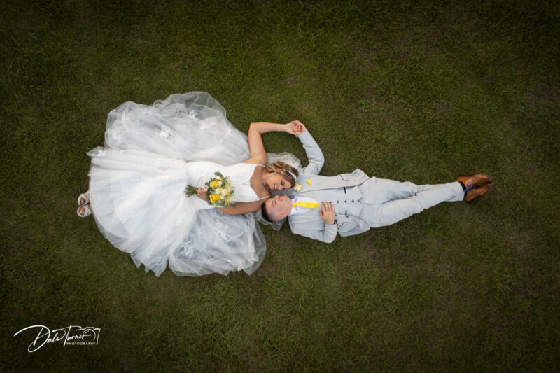 Drone photograph of bride and groom laying on the grass, looking at each other and holding hands. Taken at Carlton Towers.