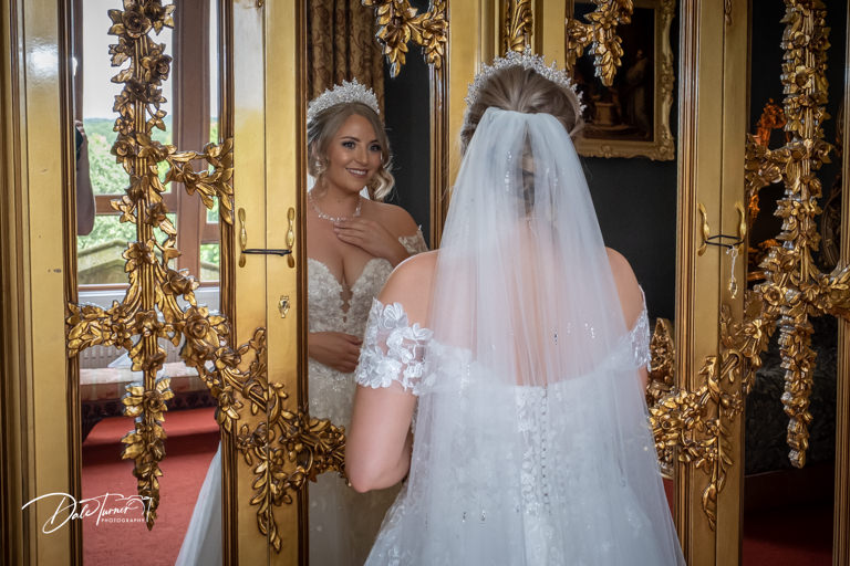 Bride looking at herself in a large, gold framed mirror, at Allerton Castle.