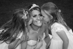 Bride bending down and being kissed by two flower girls.