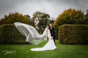 Bride and groom in the gardens of Saltmarshe Hall, with a cathedral length veil sweeping up in the air behind the bride.