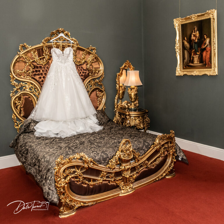 Wedding dress hung on the large, gold headboard of a very ornate bed in the bridal suite of Allerton Castle.