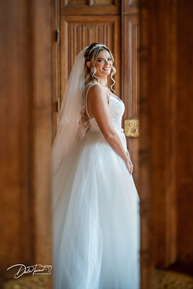 A bride through a gap in large wooden doors, at Carlton Towers.