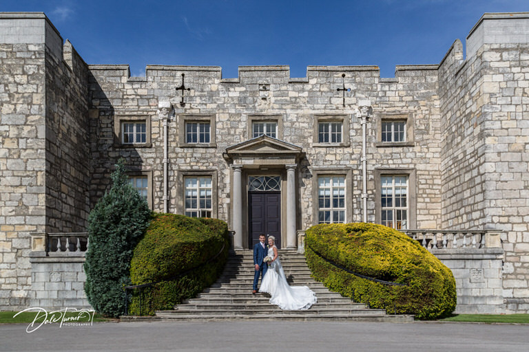 Wide image of bride and groom on the steps outside Hazlewood Castle.