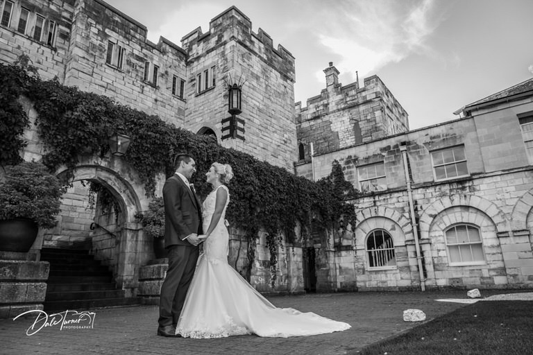 Bride and groom holding hands and looking at each other in the courtyard of Hazlewood Castle.