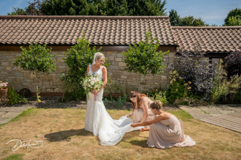 Two bridesmaids adjusting the brides dress, at Loversall Farm.