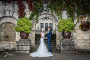 Bride and groom standing under a stone arch at Hazlewood Castle.