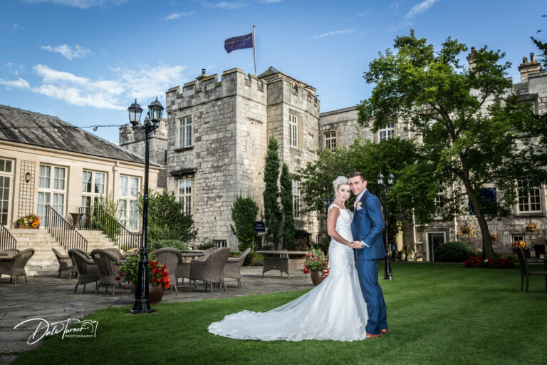 Bride and groom holding hands with Hazlewood Castle in the background.