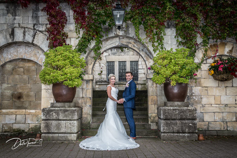 Bride and groom standing under an arch in the courtyard of Hazlewood Castle.