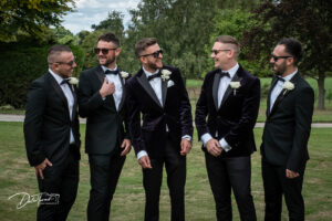 Groom, best man and groomsman all wearing sunglasses and laughing in the grounds of Saltmarshe Hall.