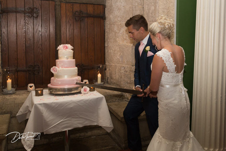Bride and groom cutting a four tier wedding cake with a broadsword at Hazlewood Castle.