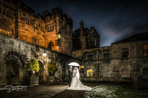 Twilight photograph of a bride and groom holding an umbrella, at Hazlewood Castle.