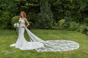 Bride standing alone with her cathedral length veil stretched out on the grass behind her.