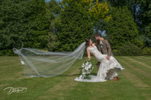 Bride and groom leaning back with a cathedral length veil sweeping behind them, in the gardens of Carlton Towers.