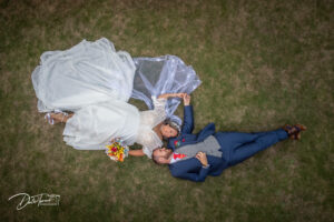 Drone photograph of a bride and groom laying on the grass, smiling and holing hands at The Parsonage, Escrick.