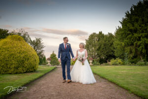 Bride and groom walking towards the camera while they hold hands and smile at each other. In the grounds of Wortley Hall, Barnsley.