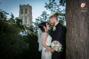 Award winning photograph of a bride and groom looking at each other in a close embrace while leaning on a tree. Howden Minster is in the background.