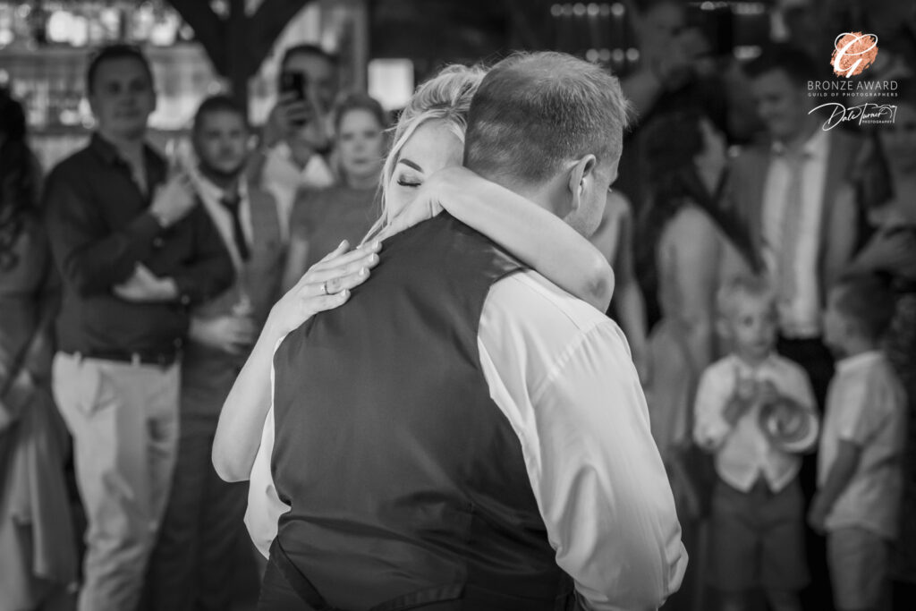 Award winning photograph of a bride and groom during their first dance. They are in a close, loving embrace while their friends and family watch them, at Loversall Farm, Tickhill.