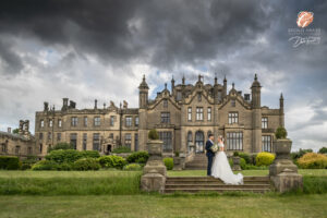 Award winning photograph of a bride and groom looking at each other on the steps with Allerton Castle in the background. Large grey storm clouds overhead.