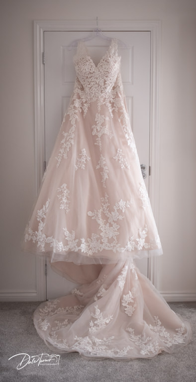 Elegant wedding dress with lace detailing hanging on door