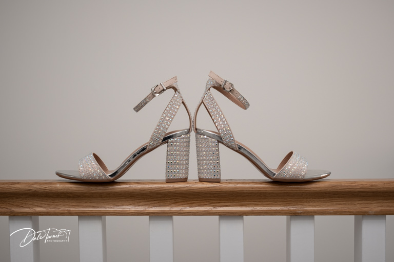 Rhinestone studded high-heel sandals on wooden railing.
