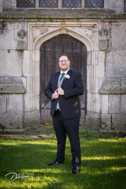 Groom smiling in suit by historical church door.