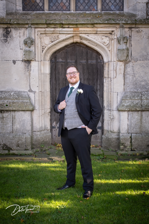 Groom smiling in front of historic stone archway.