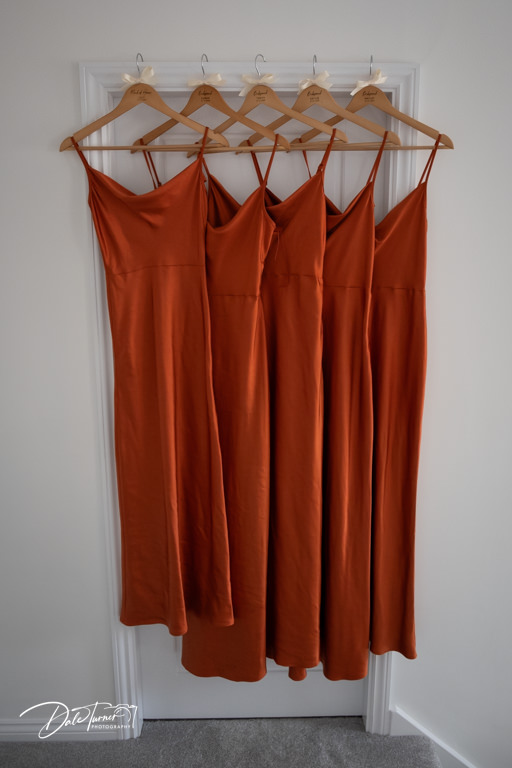 Four orange bridesmaid dresses hanging on door.