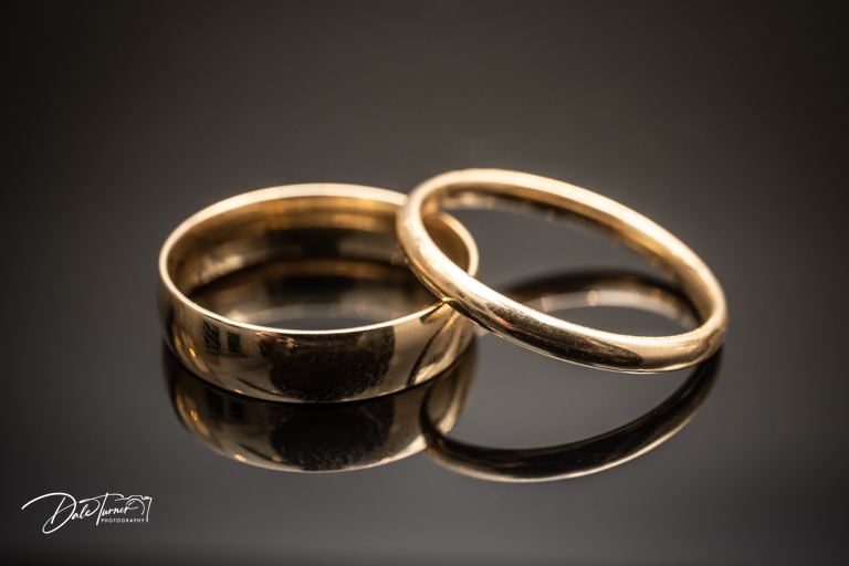 Two gold wedding rings on reflective surface.