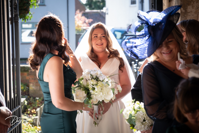 Smiling bride with bouquet and guests in church entrance.