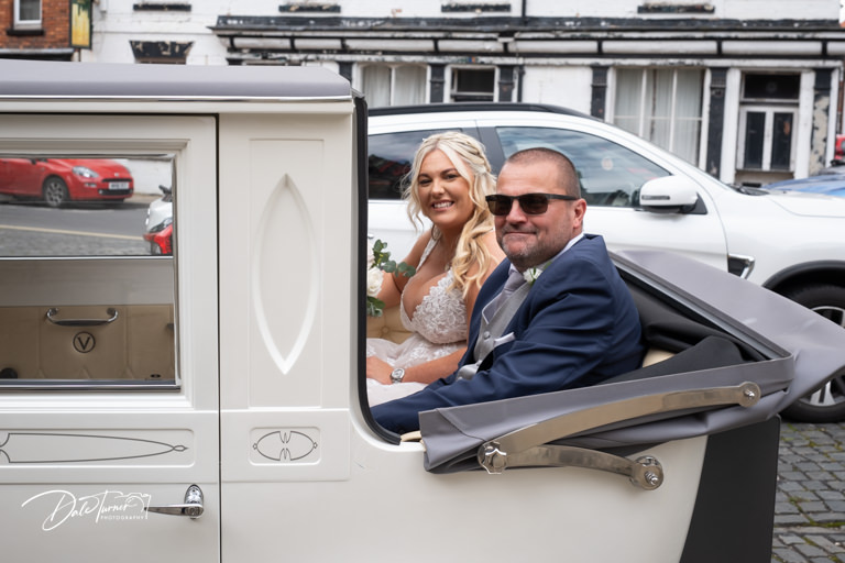 Bride and father smiling in classic wedding car.