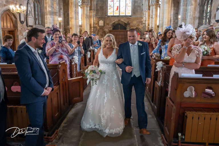 Bride walking down aisle with groom watching at Howden Minster.