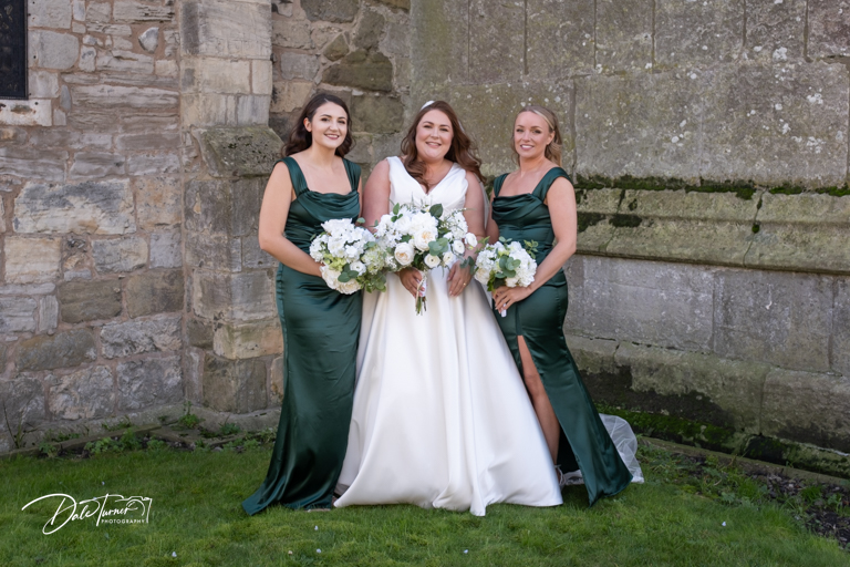 Bride with bridesmaids in green dresses holding bouquets.