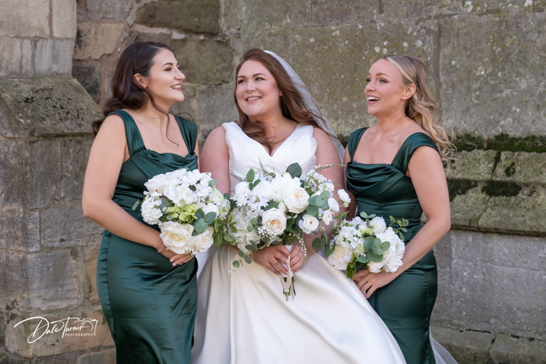 Bride is laughing with bridesmaids in green dresses holding bouquets.