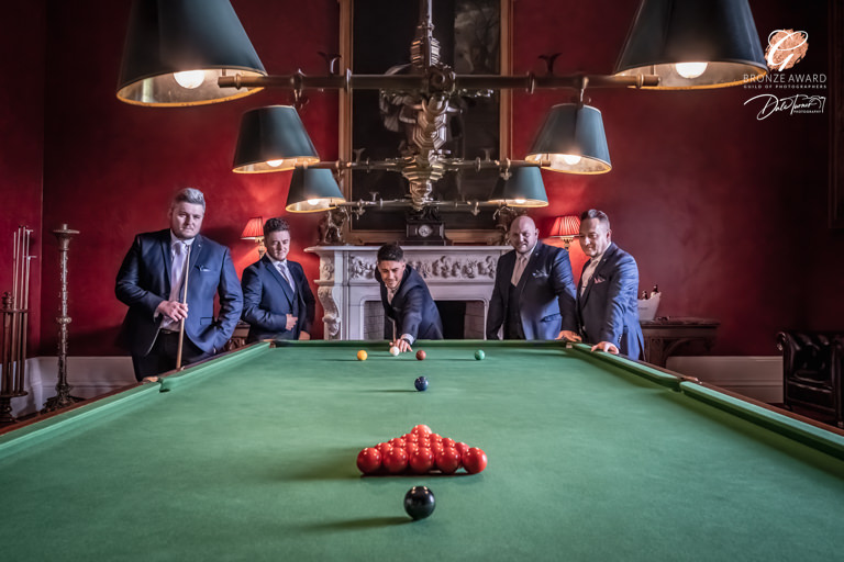Men in suits playing snooker in a traditional red room.