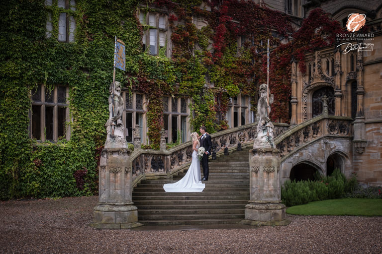 Bride and groom on ivy-covered manor staircase.