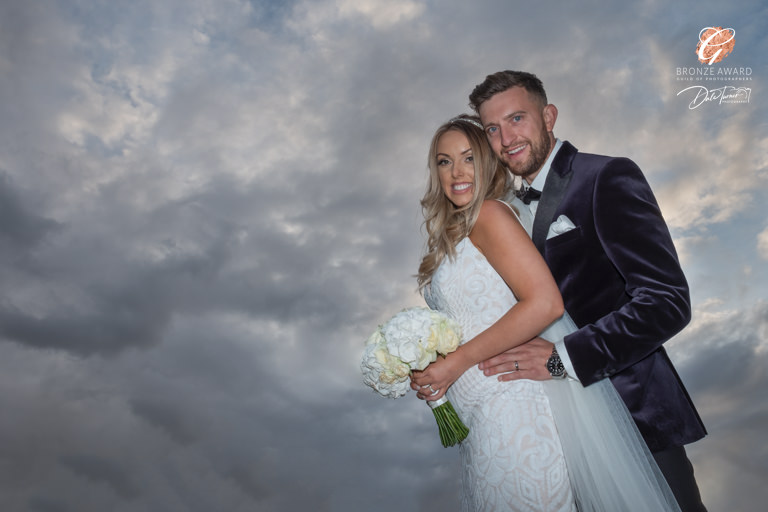 Wedding couple embracing under dramatic clouds.