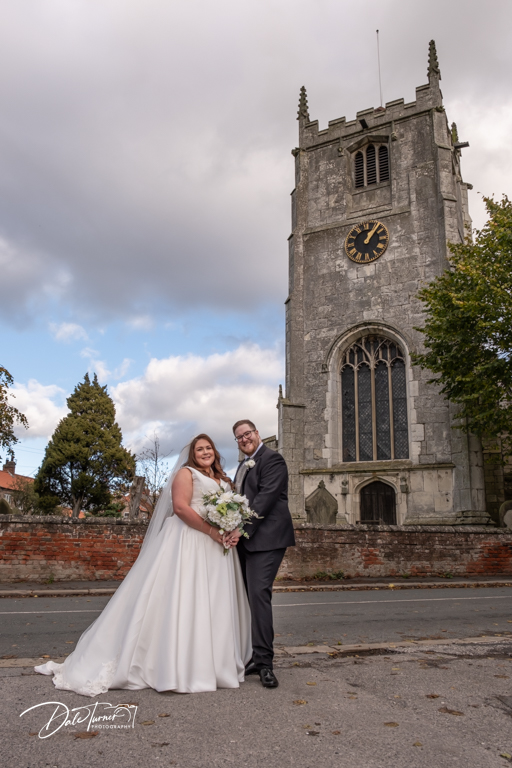 Bride and groom posing by Wistow Village All Saints Church on wedding day.
