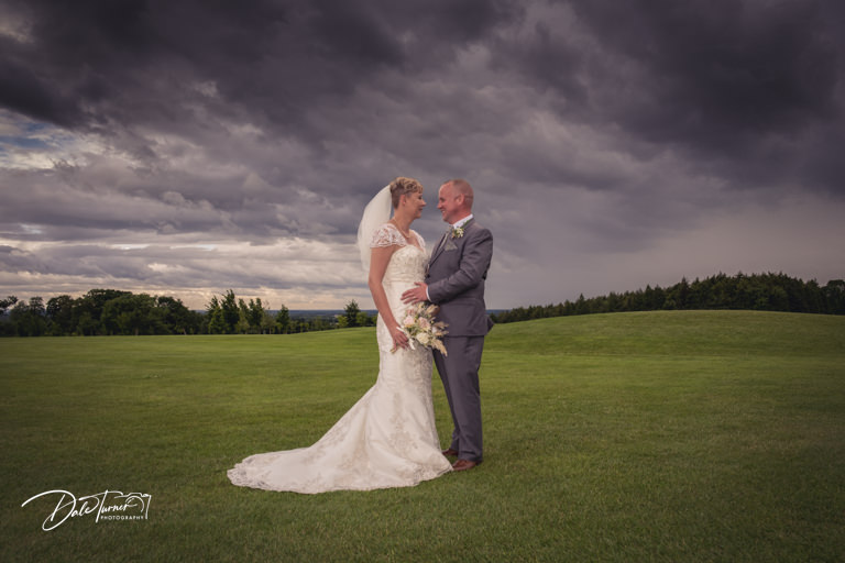 Couple embracing at wedding under stormy sky.
