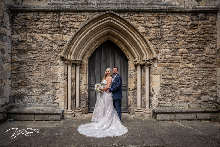 Couple posing by ancient church doorway on wedding day.