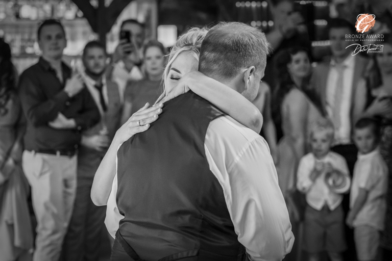 Emotional hug at wedding, guests watching, black and white photo.